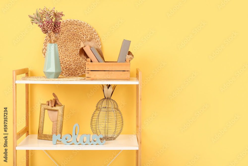 Vase with baby pineapples, books and decor on shelves near yellow wall