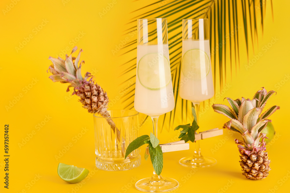 Glasses of cocktail with lime, mint and baby pineapples on yellow background