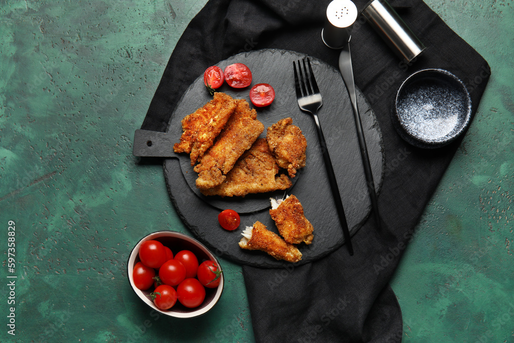 Boards of tasty fried codfish on green background