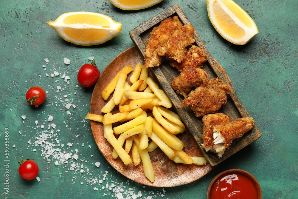 Plate of tasty fried codfish with french fries on green background