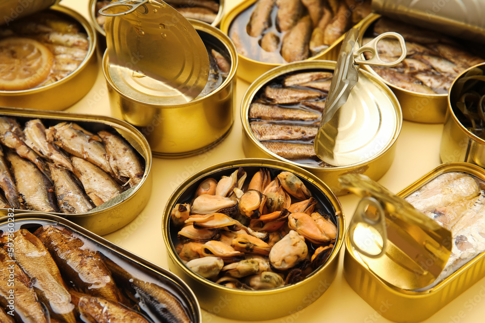 Many opened tin cans with different fish on beige background