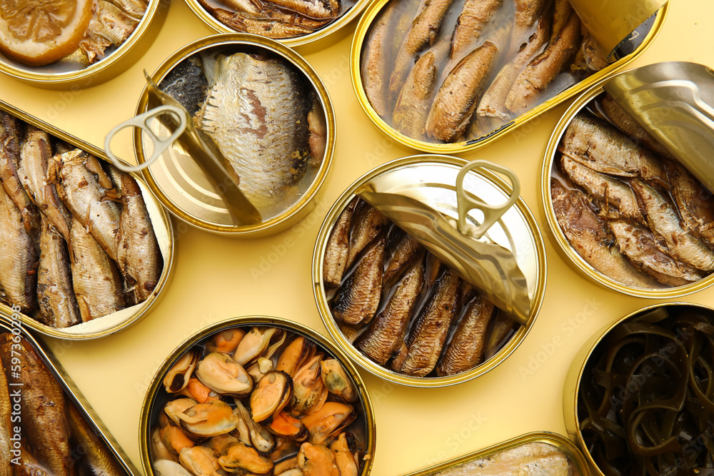 Many opened tin cans with different fish on beige background