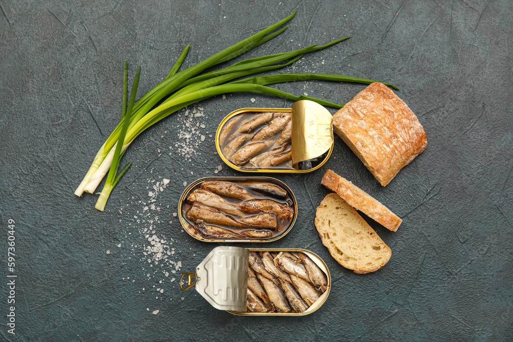 Opened tin cans with sprats in oil, green onion and bread on black table