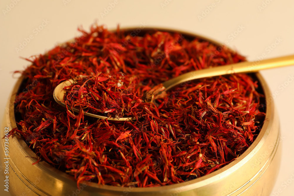 Golden bowl and spoon with pile of saffron on light background