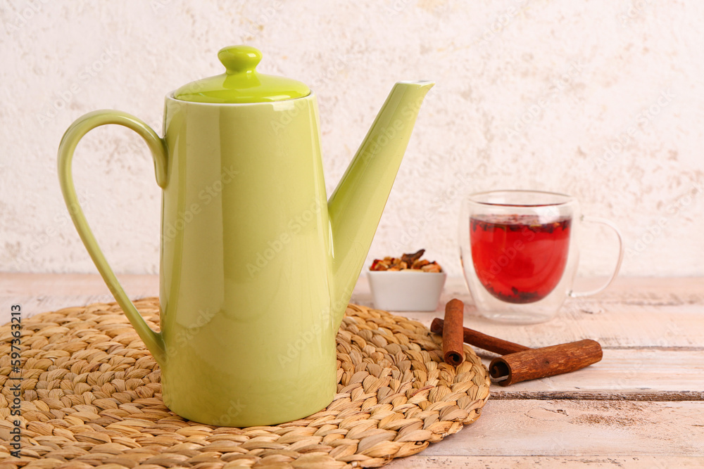 Wicker mat with teapot and cup of fruit tea on white wooden table