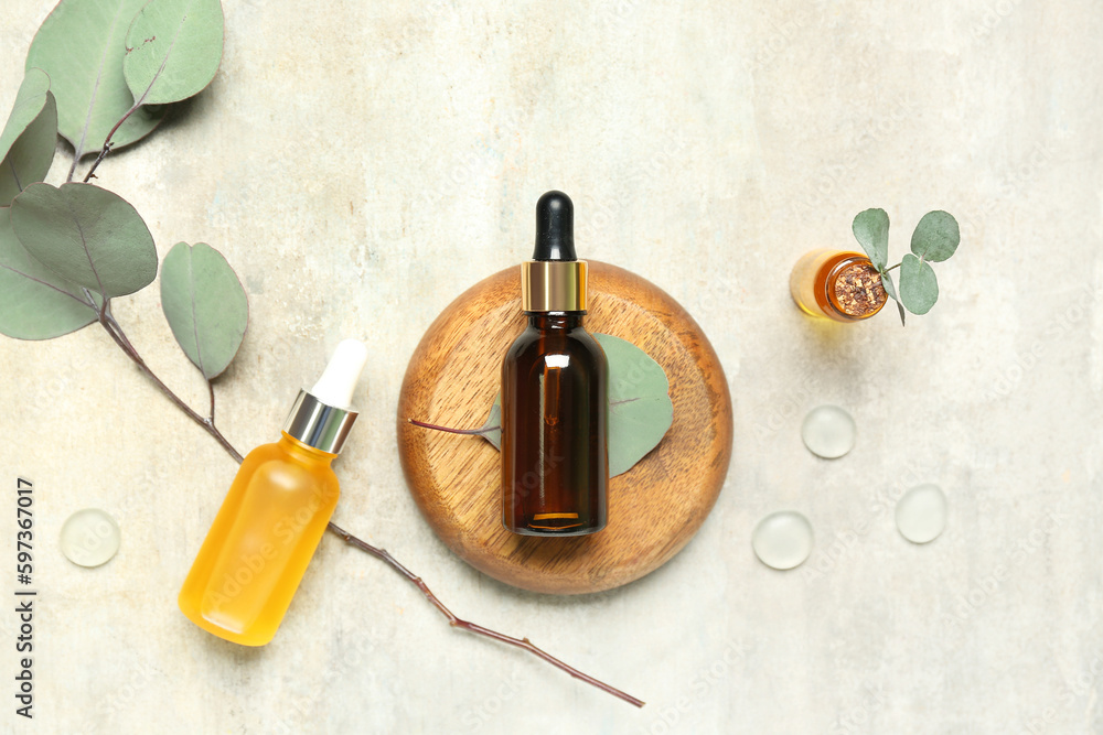 Cosmetic oil bottles with wooden stand and eucalyptus branch on textured background