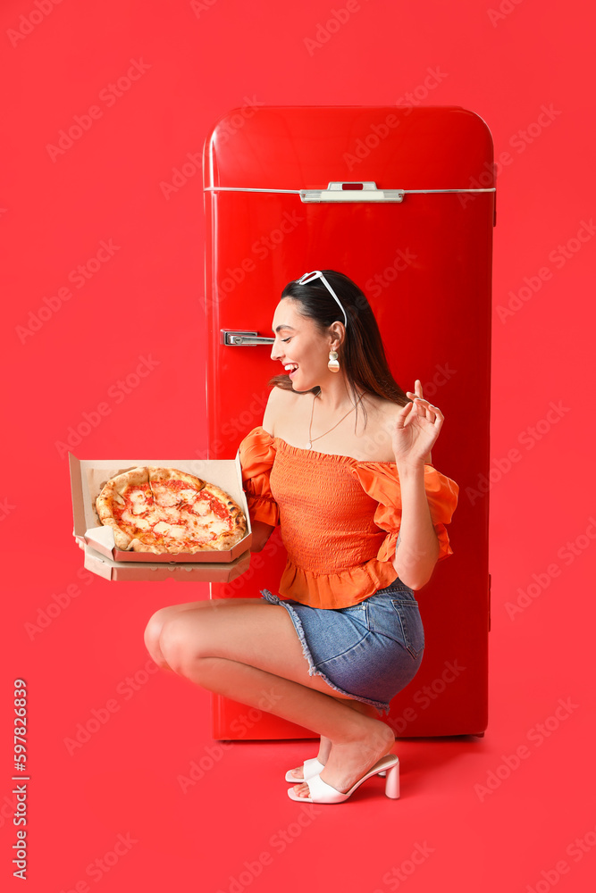 Beautiful woman with tasty pizza and fridge on red background