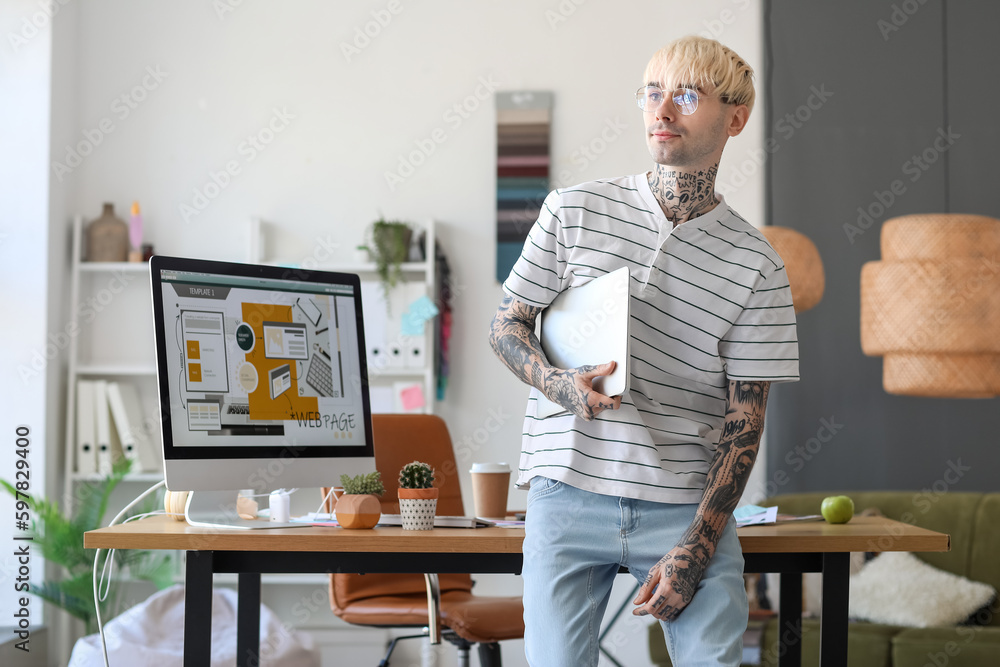 Tattooed graphic designer with laptop in office