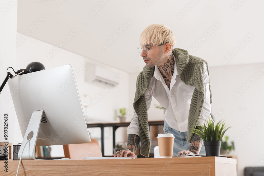 Young tattooed man working with computer in office