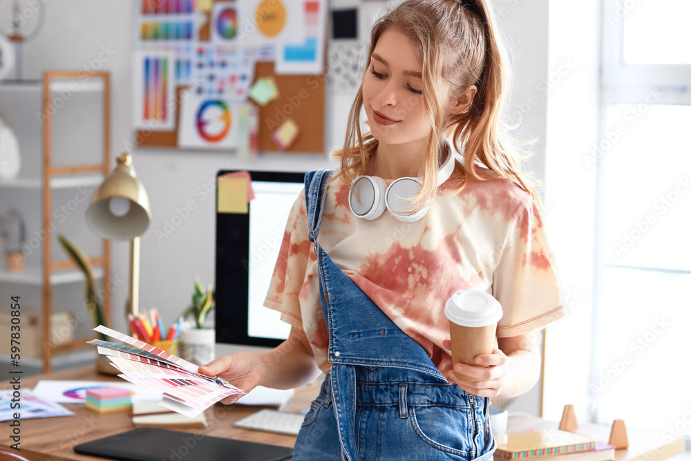 Female graphic designer with cup of coffee and color palettes in office