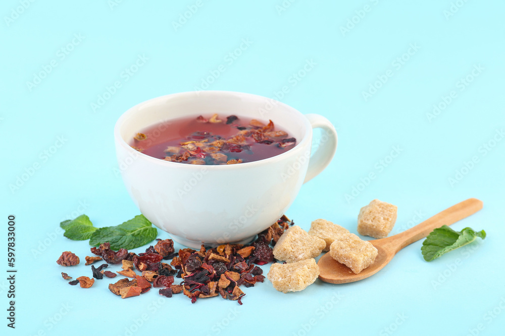 Glass of fruit tea, wooden spoon and snacks on blue background