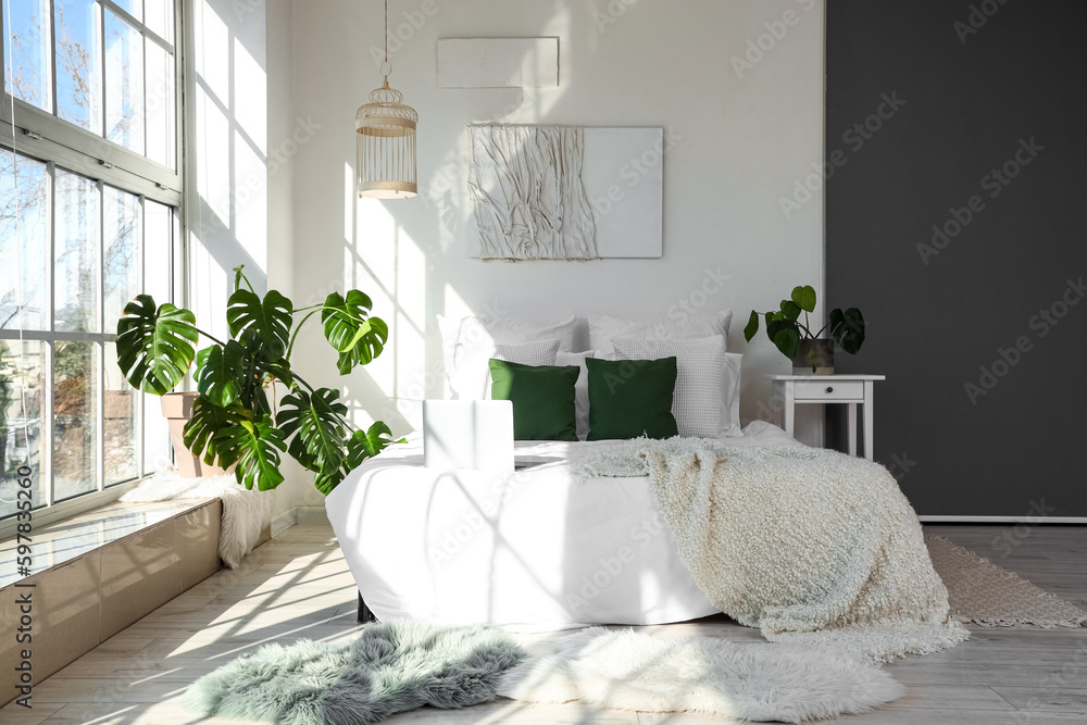 Interior of light bedroom with Monstera houseplant and bed