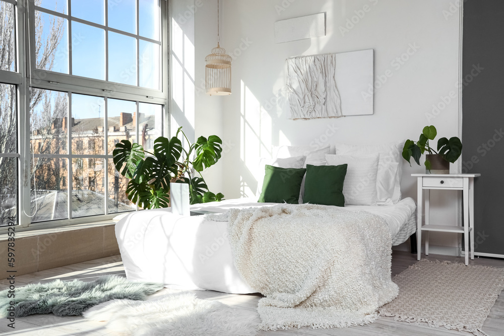 Interior of light bedroom with Monstera houseplant and bed