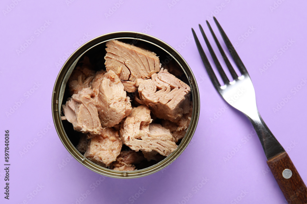 Opened tin can with delicious tuna and fork on lilac background