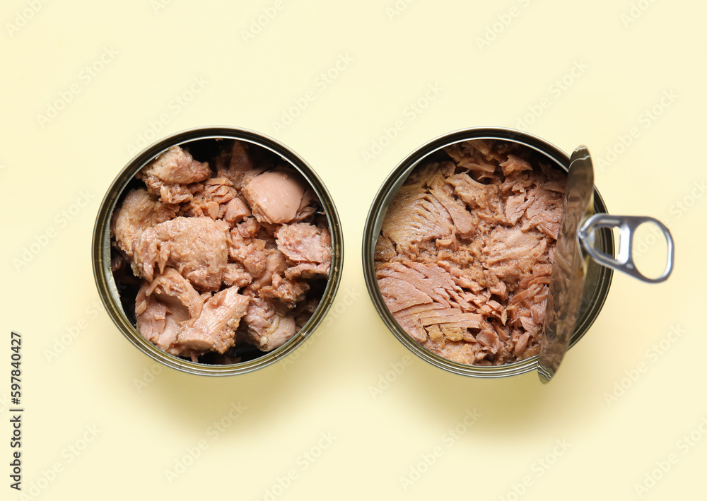 Opened tin cans with delicious tuna on beige background