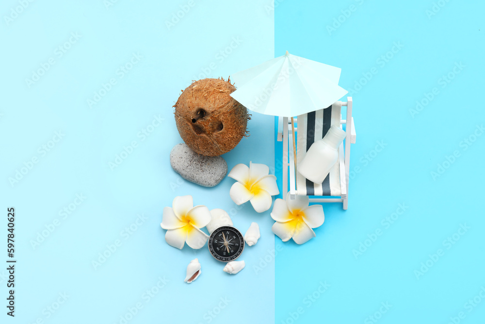 Composition with miniature deck chair, umbrella, sunscreen and coconut on blue background