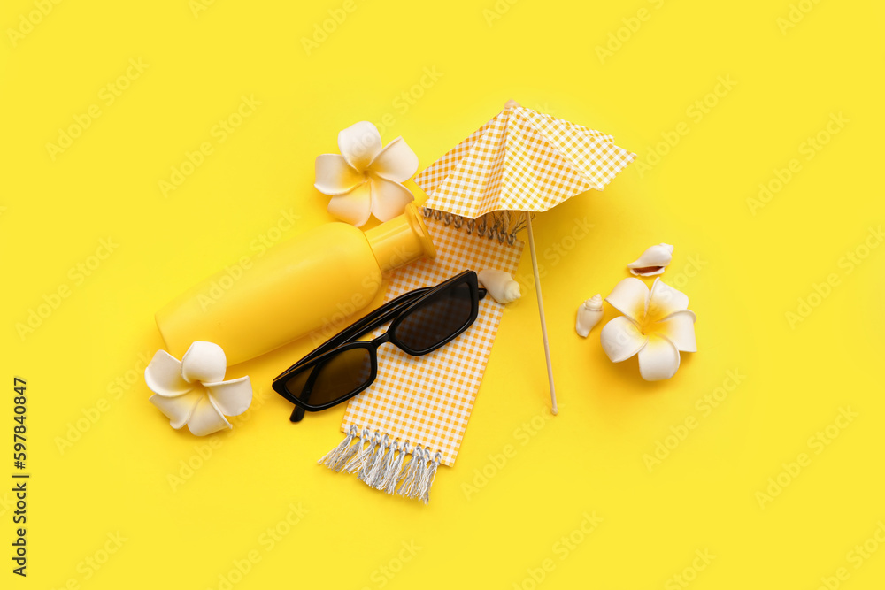 Composition with sunglasses, bottle of sunscreen, plumeria flowers and umbrella on yellow background