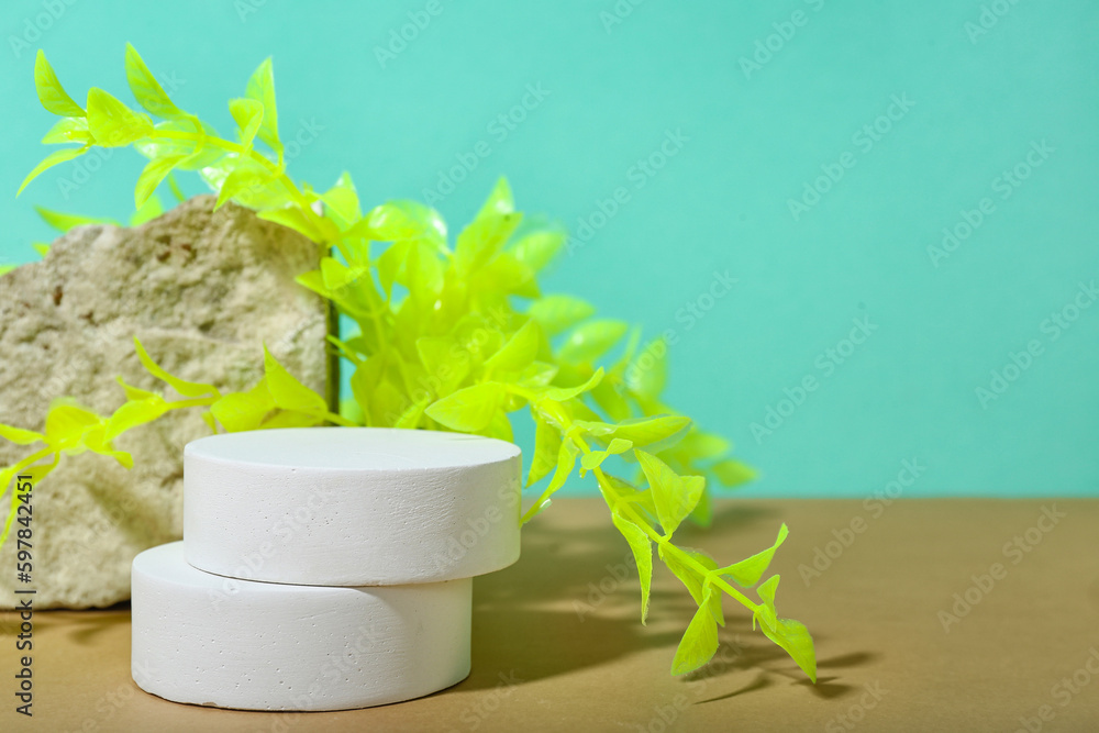 Decorative plaster podiums, seaweed and stone in sand on turquoise background