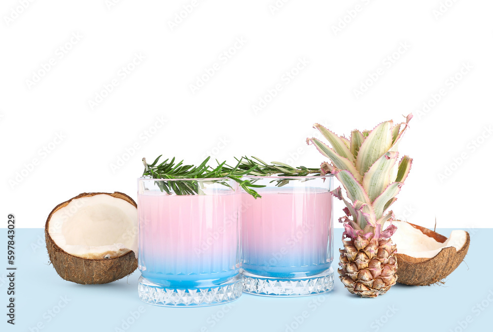 Glasses of cocktail with rosemary, coconut and baby pineapple on table near white wall