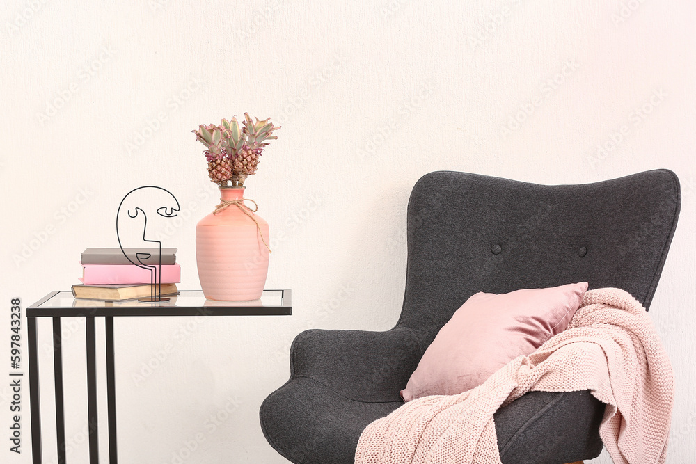 Vase with baby pineapples, books on table and armchair in living room