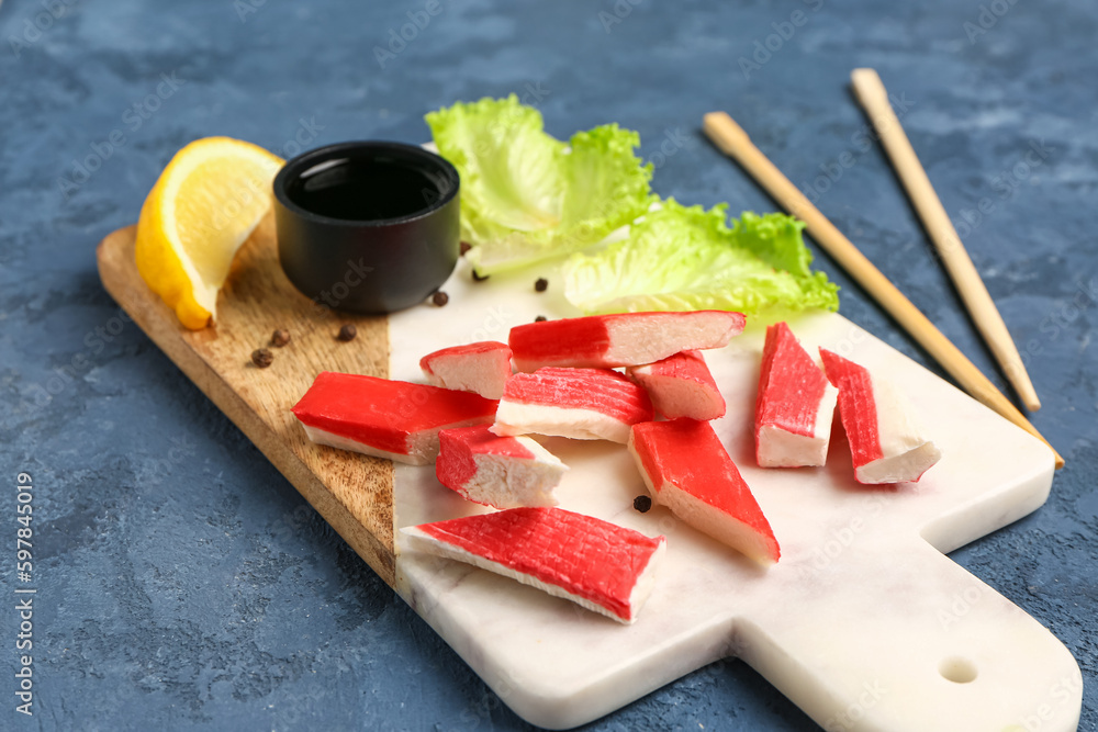 Board with tasty crab sticks on blue background