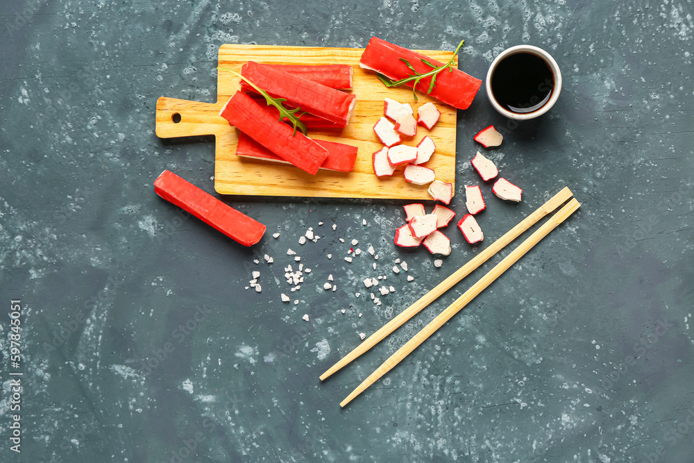 Wooden board with tasty crab sticks and sauce on green background