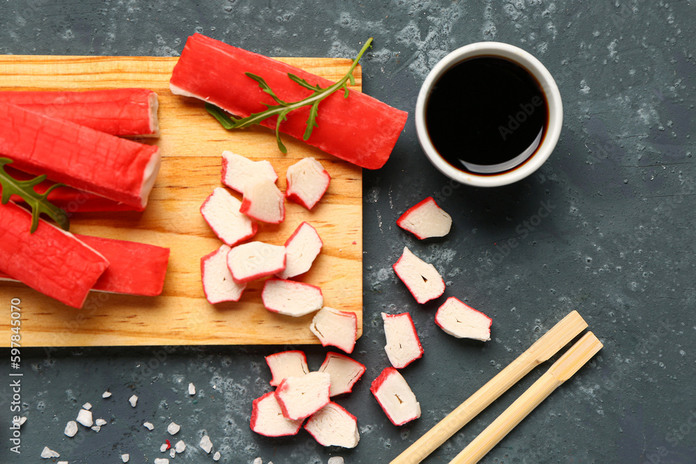 Wooden board with tasty crab sticks and sauce on green background, closeup