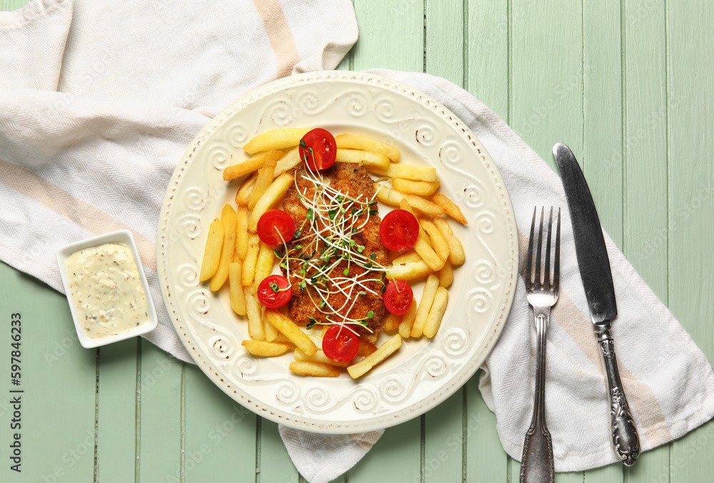 Plate of tasty fried codfish with french fries and sauce on green wooden background