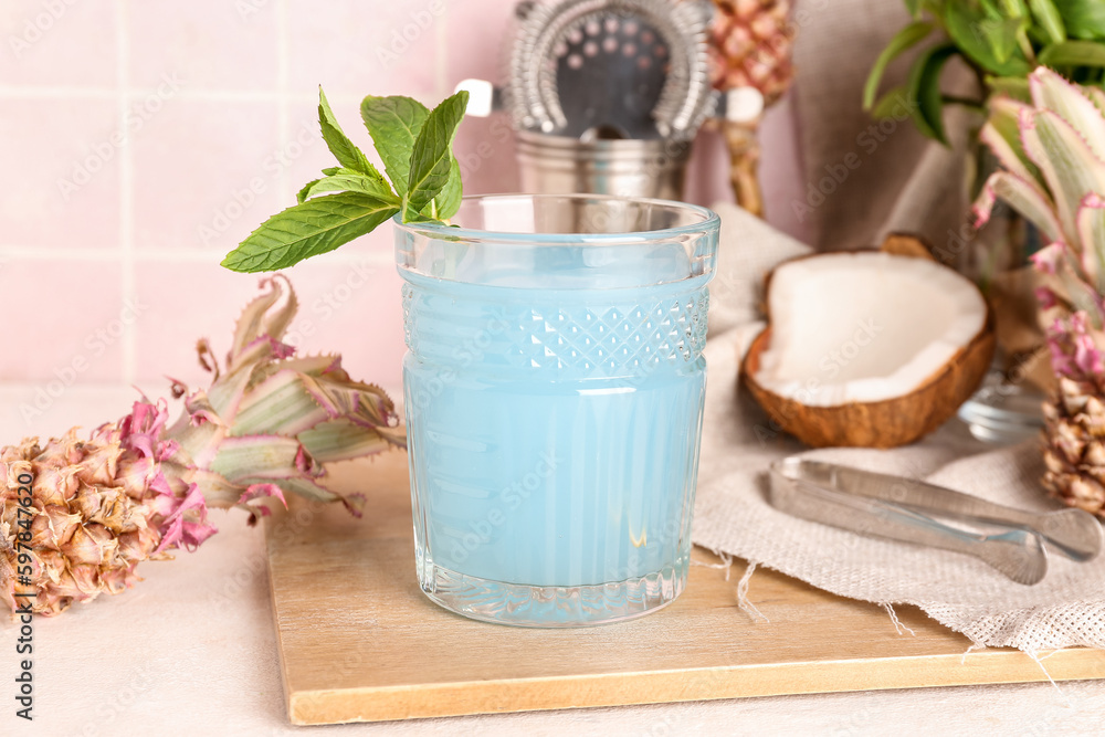 Glass of cocktail with mini pineapples on table near pink tile wall, closeup