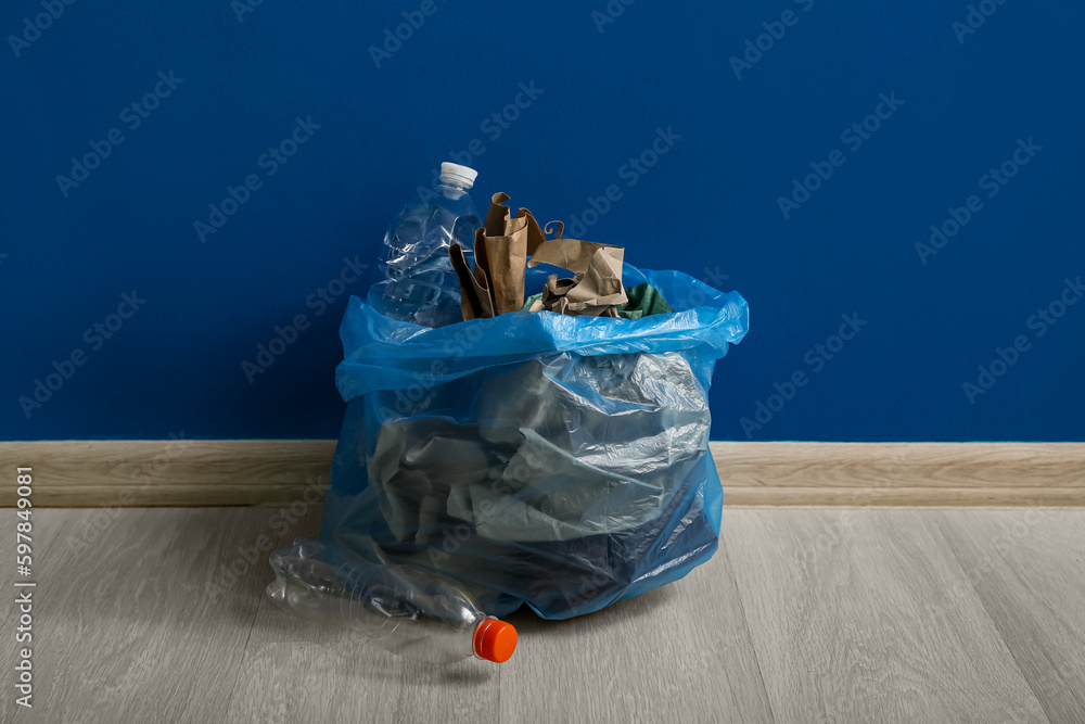 Full garbage bag near blue wall