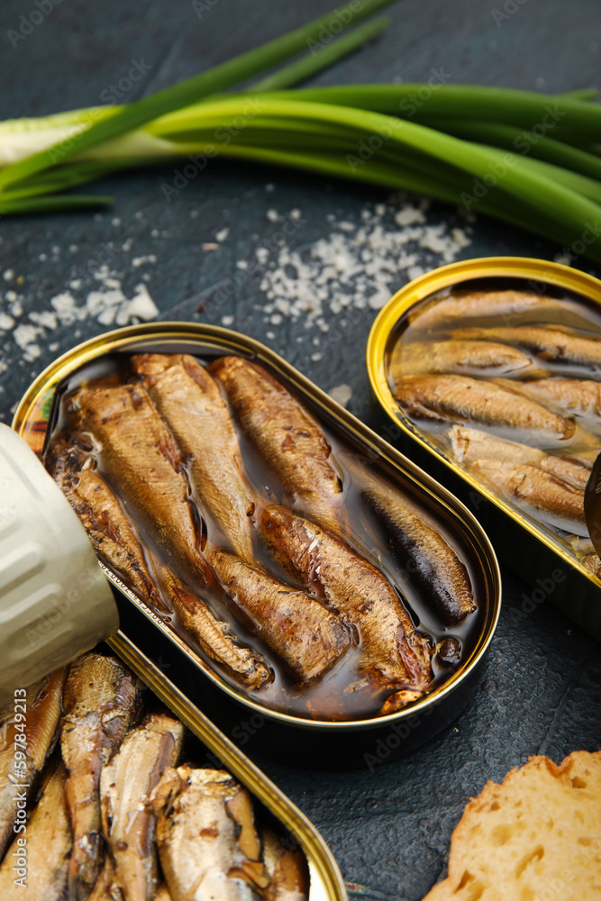 Opened tin cans with sprats in oil on black table