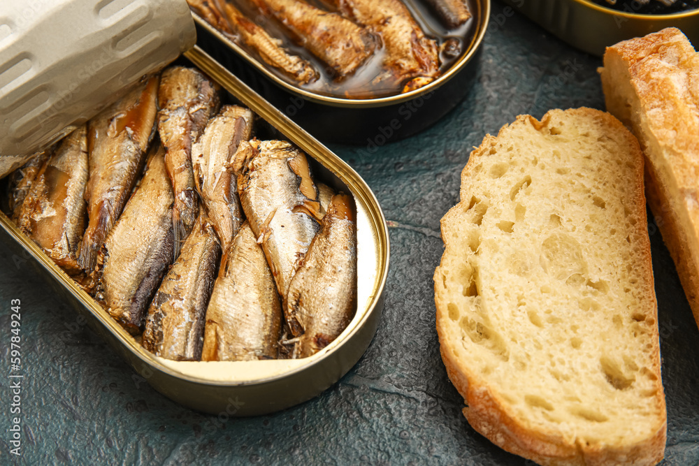 Opened tin cans with sprats in oil and bread on black table