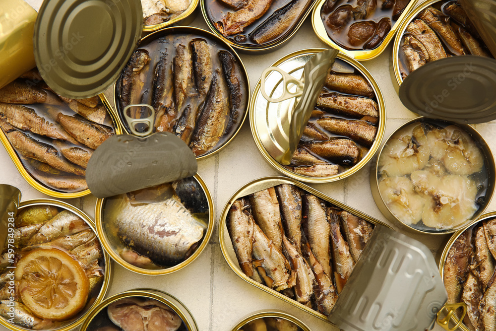 Many opened cans with different fish on tiled table, closeup