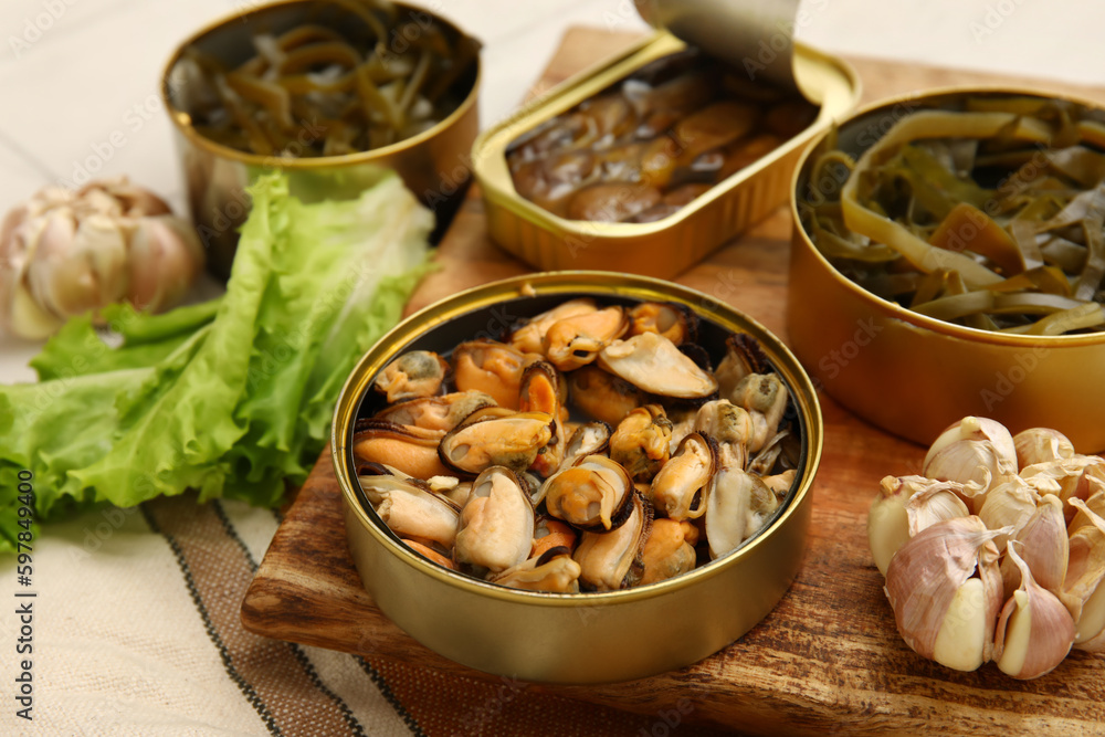 Board with opened tin cans of mussels and seaweed, closeup