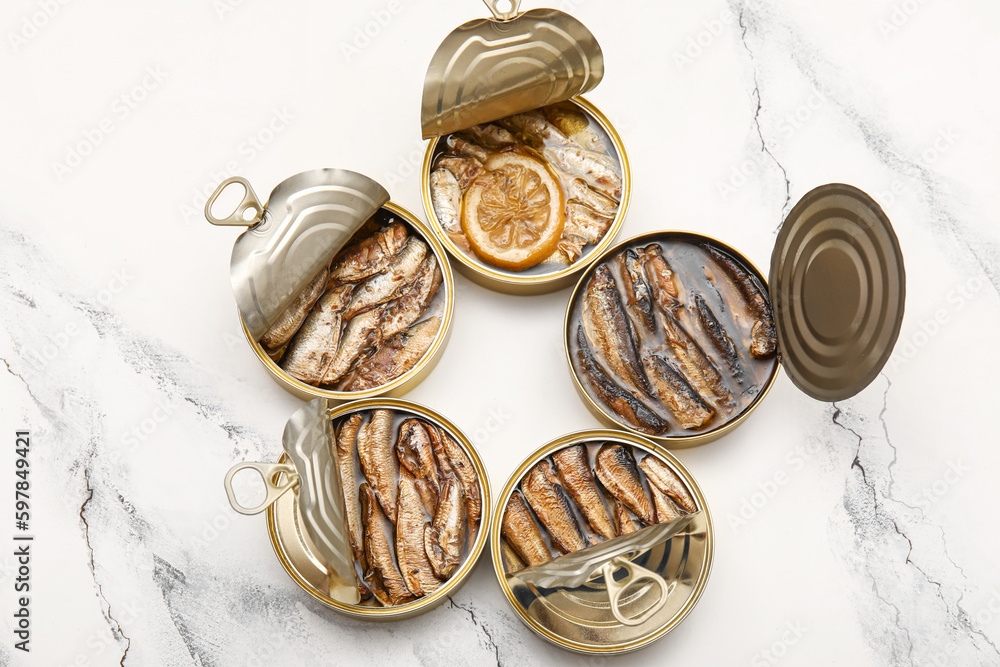 Opened tin cans with sprats in oil on white marble table