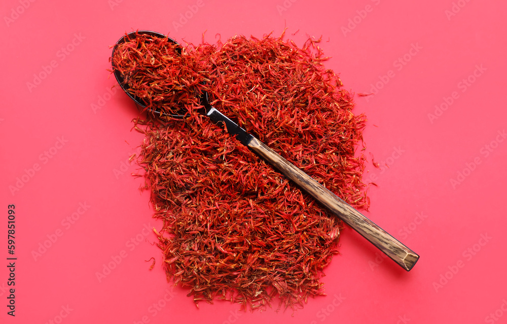 Spoon with pile of saffron on red background