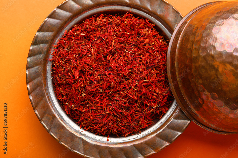 Bowl with pile of saffron on orange background