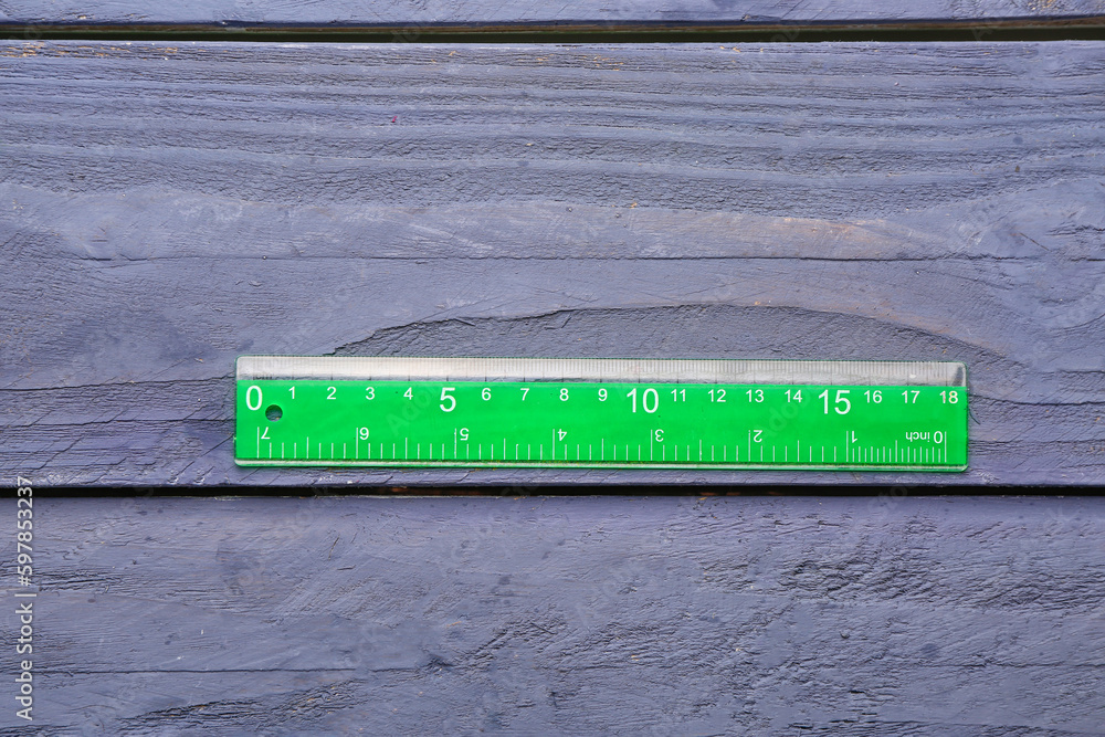 Green plastic ruler on blue wooden background