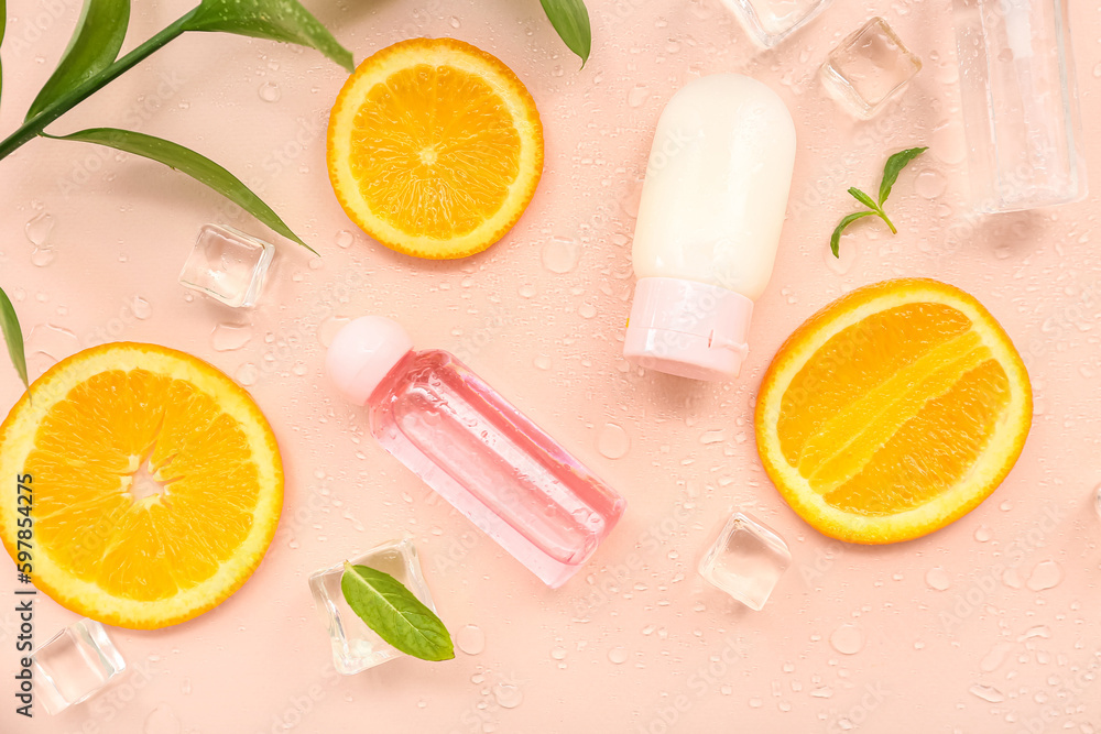 Cosmetic bottles with orange slices, ice cubes and mint on beige background