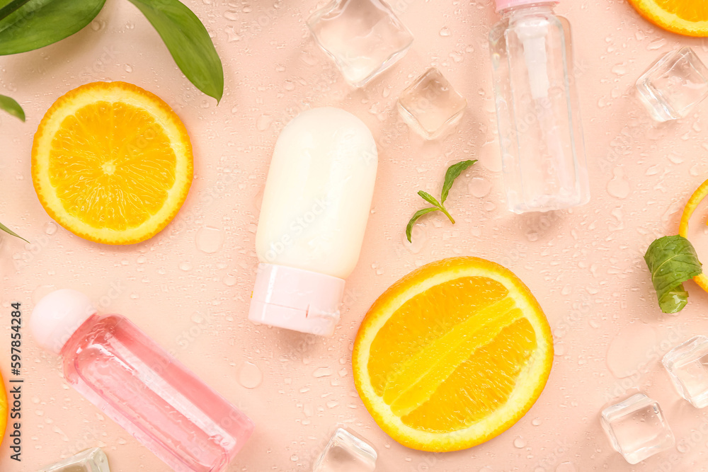 Cosmetic bottles with orange slices, ice cubes and mint on beige background