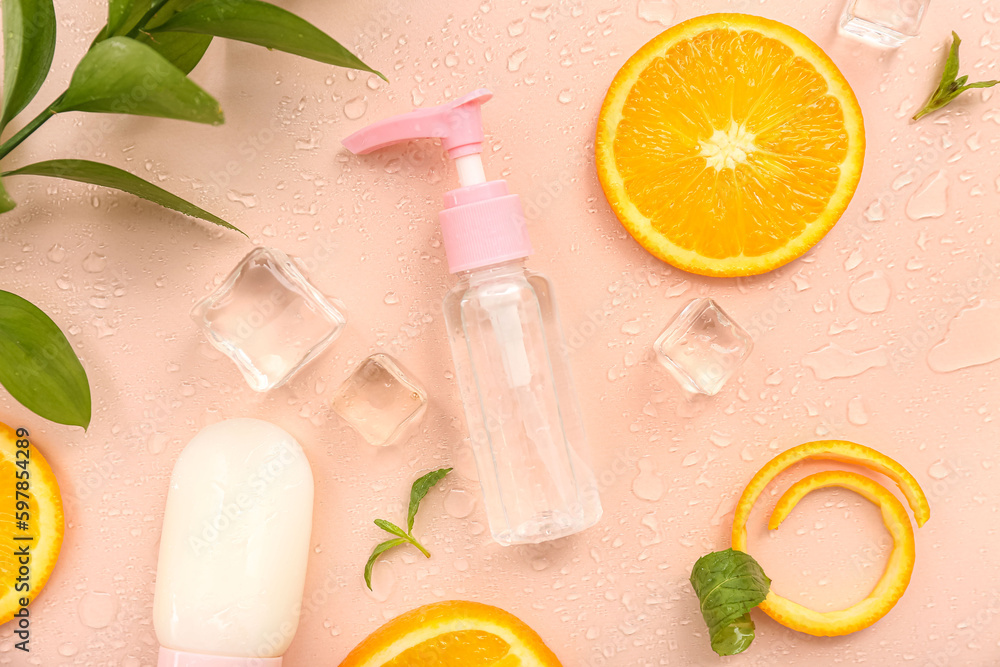 Cosmetic bottles with orange slices, ice cubes and mint on beige background