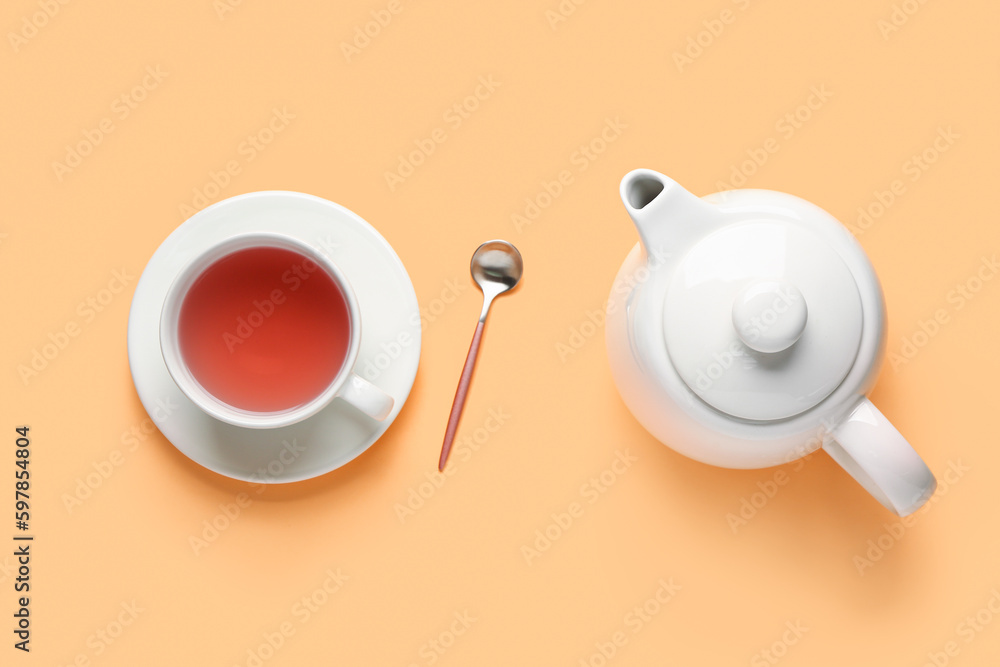 Ceramic teapot and cup of tea on orange background