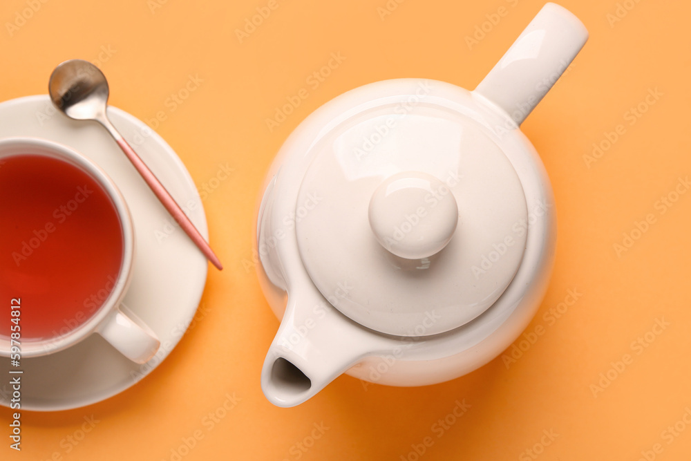 Ceramic teapot and cup of tea on orange background