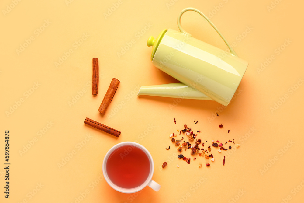 Stylish ceramic teapot and cup of tea on orange background