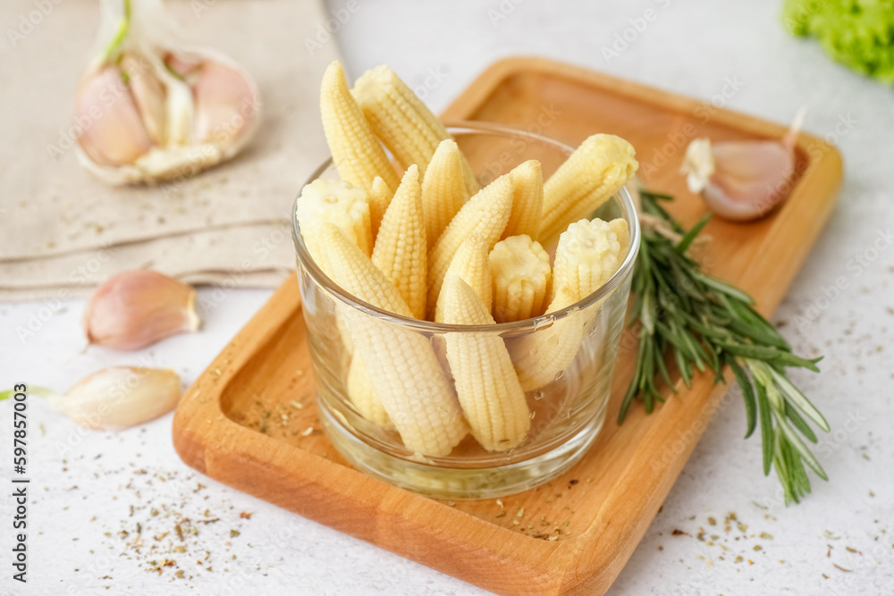 Glass with tasty canned corn cobs on light background