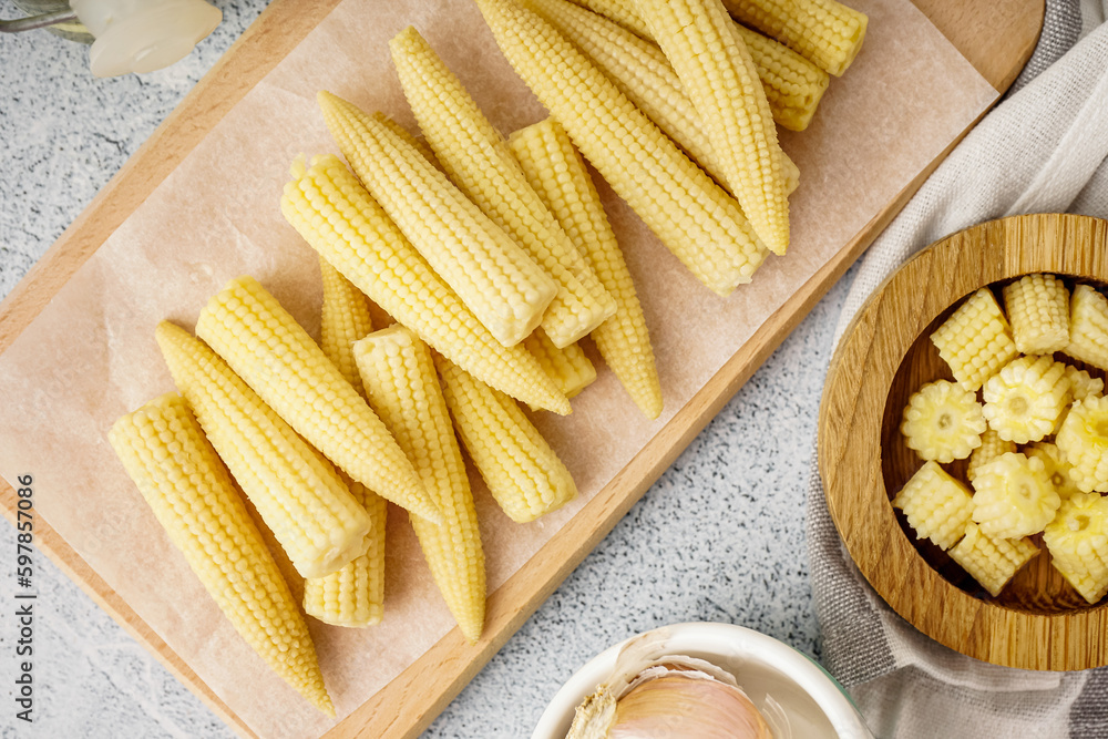 Wooden board with tasty canned corn cobs on light background