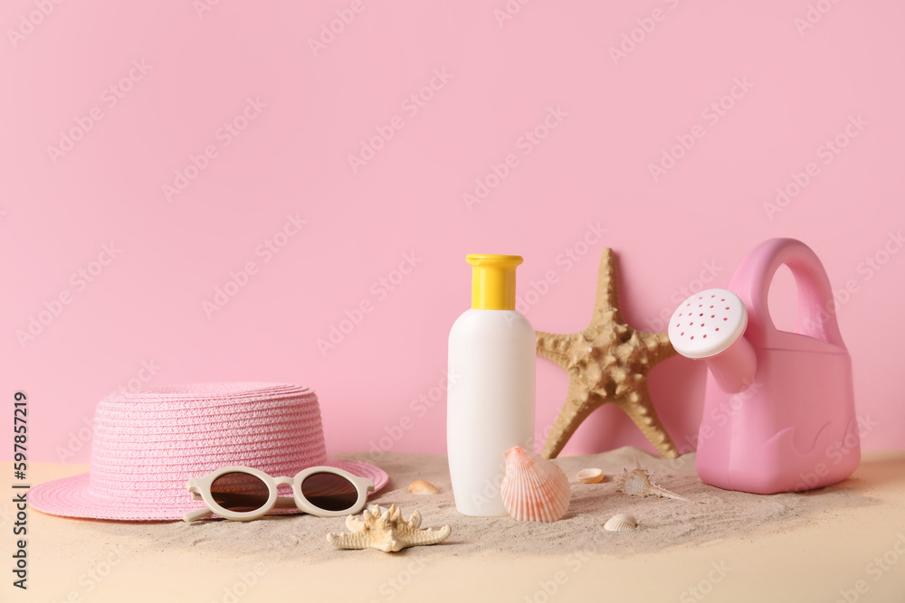 Sunscreen cream for baby with beach accessories on sand near pink wall