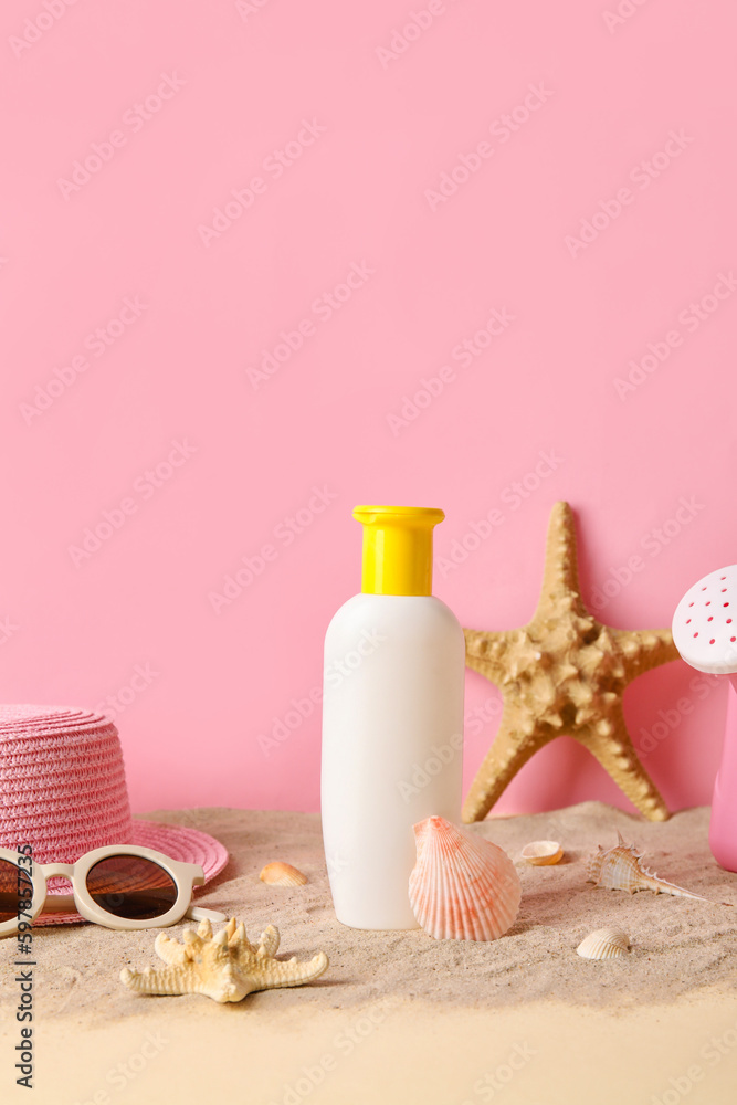 Sunscreen cream for baby with beach accessories on sand near pink wall