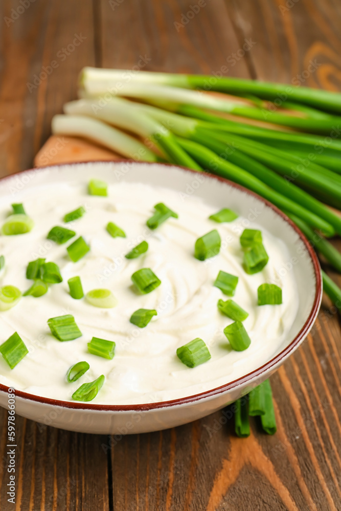 Bowl of tasty sour cream with green onion on wooden background, closeup