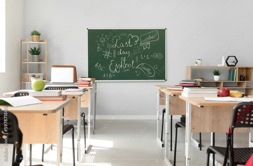 Blackboard with text LAST DAY OF SCHOOL and drawings on light wall in classroom